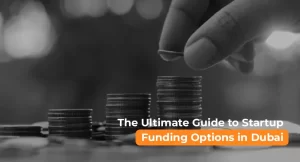 Stacked coins and hand placing a coin, representing startup funding options available for new businesses in Dubai.