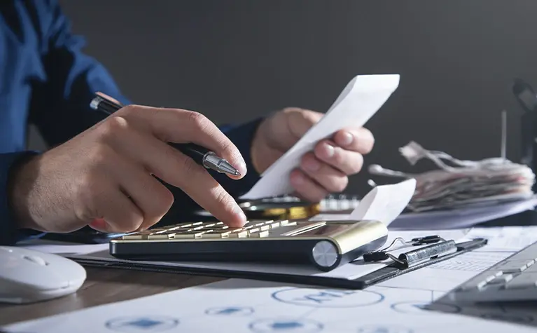 Person calculating business startup costs with receipts and financial documents on desk
