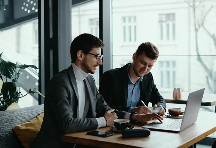 Two entrepreneurs discussing expansion plans over a laptop in a modern cafe setting